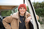 Happy young woman in knit hat at camper van doorway