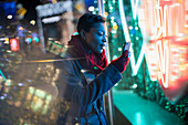 Young woman with smartphone at neon storefront sign at night