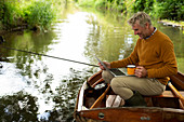 Man fly fishing and using laptop with coffee in a boat