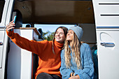 Young women friends taking selfie in camper van doorway