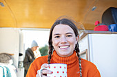Happy young woman drinking tea in camper van doorway