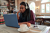 Businesswoman with headphones working at laptop in cafe