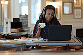 Woman with headphones drinking coffee at laptop in cafe
