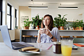 Happy woman drinking coffee at laptop in office lounge