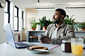 Thoughtful man with coffee working at laptop in office