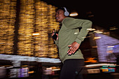 Woman with headphones jogging below city lights at night
