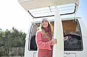 Happy female surfer with surfboard at back of camper van