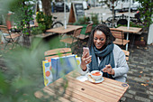 Woman using smartphone and eating soup at cafÃ© patio table