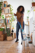 Happy young woman mopping hardwood floor in apartment