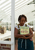 Plant nursery owner with open sign in greenhouse doorway