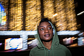 Young woman in hoodie wearing headphones under city lights