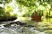 Man with coffee fly fishing and writing in boat on river
