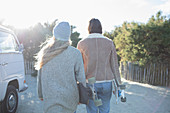 Young women friends with skateboards walking on beach path