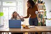 Daughter serving coffee to mother working at laptop