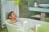 Woman enjoying bubble bath with candles in luxury bathroom