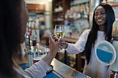 Female bartender serving woman white wine at bar counter