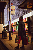 Woman with Christmas shopping bags on city sidewalk at night