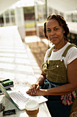 Confident female garden shop owner at laptop in greenhouse