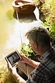 Man fly fishing and video chatting with tablet at riverbank
