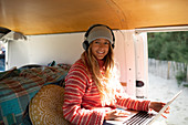 Happy young woman with headphones and laptop in camper van