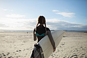 Young female surfer with braids and surfboard on sunny beach