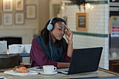 Tired businesswoman with headphones working at laptop