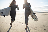 Young female surfers running on beach with surfboards