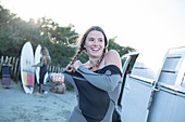 Female surfer putting on wet suit at camper van on beach