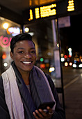 Happy young woman with smartphone on city sidewalk at night