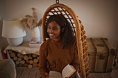 Happy woman with headphones reading book in hanging chair