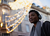 Young woman with headphones below building with lights