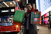 Happy young woman with Christmas gifts in city at night