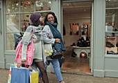 Mother and daughter with shopping bags walking arm-in-arm