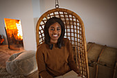 Happy young woman reading book in hanging rattan chair