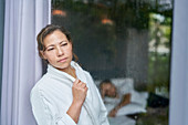 Curious woman in bathrobe looking out rainy window