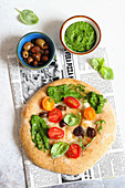 Pizza with mozzarella, pesto, olives and tomatoes