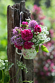 A bouquet of roses, Caucasian crossword and ground elder in a cup hung on a post