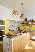 Kitchen island in marble and pale wood in open-plan kitchen with yellow accent wall