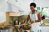 African American woman mixing salad in kitchen