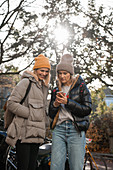 Zwei Frauen in Herbstbekleidung schauen auf ihr Smartphone