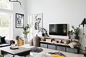 Vintage metal boxes, above wooden shelves and TV, posters on a white wall in a living room