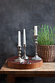 Silver candle holders on a wooden disc and thyme in a basket