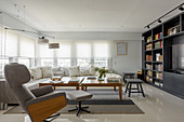 Comfortable armchair with footstool, sofa and tables in front of fitted cabinets with bookshelves and TV