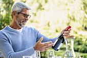 Älterer Mann betrachtet Rotweinflasche am gedecktem Tisch im Freien