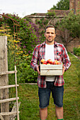 Proud man with crate of fresh harvested apples in garden