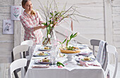 Young woman arranging a bouquet of flowers on a spring table set with hors d'oeuvres