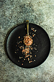Cooking concept with vintage spoon with pink salt on black wooden plate