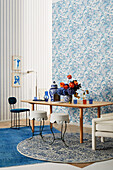 Vase of flowers on table and various seating in front of wall with blue and white wallpaper