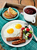 Breakfast sausage with fried eggs and fruits, served with toast and rosehips tea
