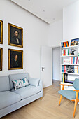 Light upholstered sofa, portrait painting above, bookshelf and armchair in reading room
